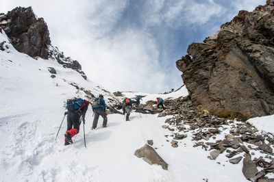 Low angle view of people hiking on snow covered mountains against sky