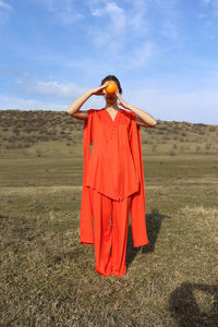 Full length of woman holding fruit while standing on field against sky