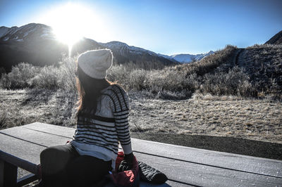 Rear view of woman sitting on bench against sky