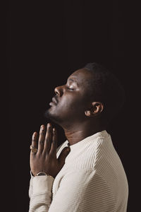 Side view of man with hands clasped by black background