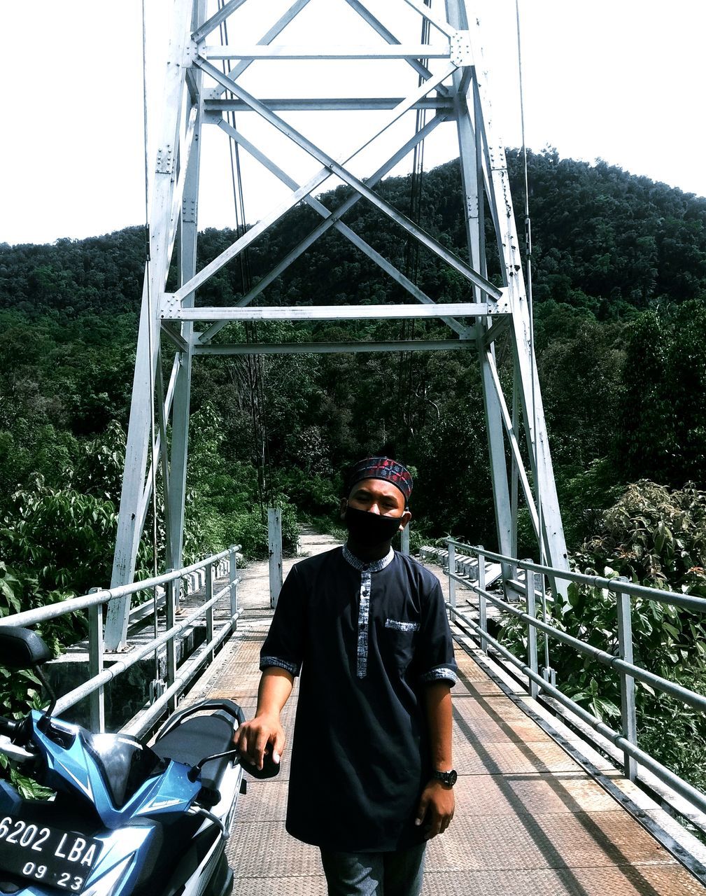 MAN STANDING ON FOOTBRIDGE AGAINST TREES