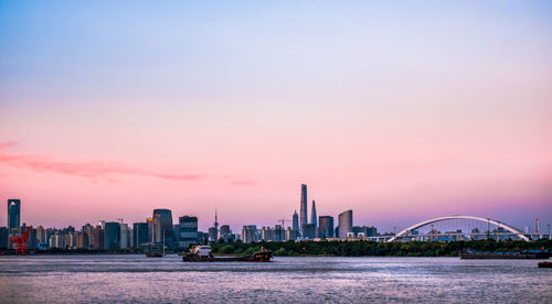 Scenic view of river by buildings against sky during sunset