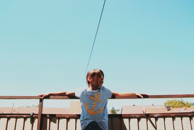 Low angle view of girl leaning on railing against clear blue sky