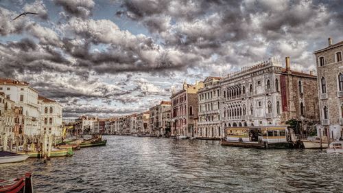 Panoramic view of canal in city against cloudy sky