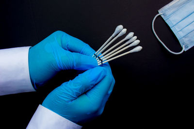 Cropped hands of surgeon holding cotton swabs against black background