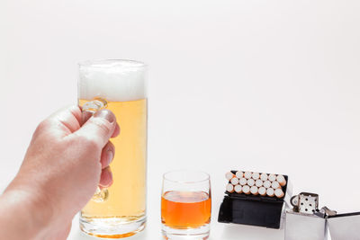 Midsection of person holding beer glass against white background