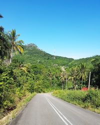 Road amidst trees against clear blue sky