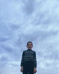 Low angle portrait of smiling boy standing against cloudy sky