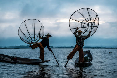 People fishing in lake against sky