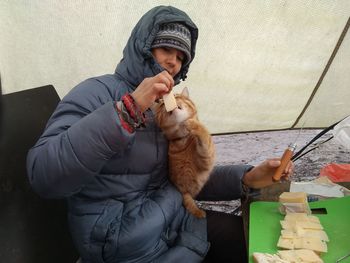 Woman wearing warm clothing feeding cheese to cat outdoors