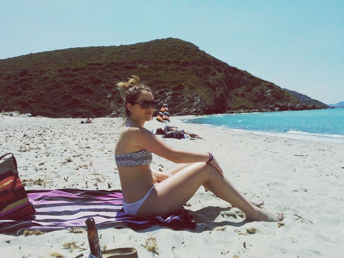 beach, young adult, lifestyles, sitting, relaxation, leisure activity, young women, sea, water, vacations, sand, full length, shore, mountain, casual clothing, clear sky, person, tranquility