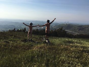 Rear view of naked friends with arms outstretched standing on field