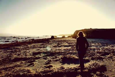 Rear view of silhouette woman standing on beach against clear sky