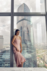 Woman in a nightgown stands at the window in a skyscraper near the bed