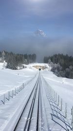 Railroad tracks by snow covered mountains against sky