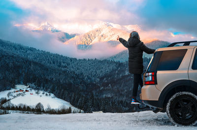 Man on land vehicle pointing to snowcapped mountain at sunset during winter