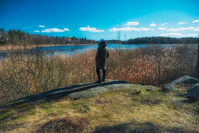 Rear view of man standing by lake against sky