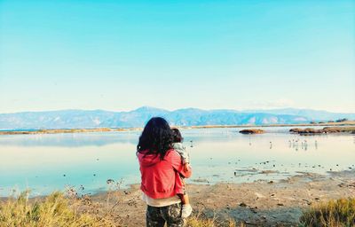 Rear view of woman standing on lake against sky