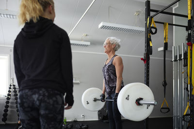 Mid adult woman looking at senior woman lifting weights