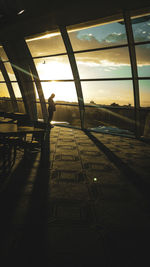 Silhouette person standing by window against sky during sunset