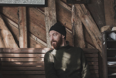 Young man looking away while standing on wood