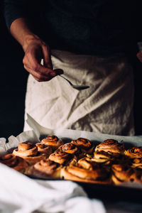 Midsection of baker pouring liquid on cinnamon buns in bakery