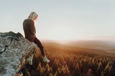 Woman sitting on rock against landscape