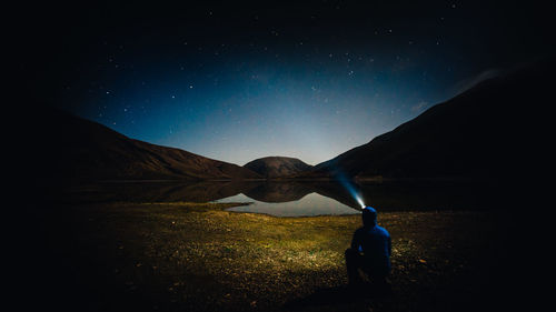 Rear view of man with flashlight against star field at night