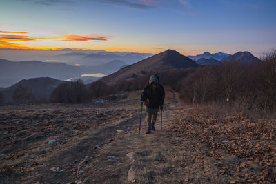 Rear view of man walking on mountain against sky during sunset