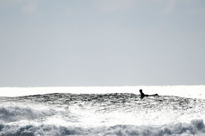 Silhouette man surfing on sea shore against clear sky