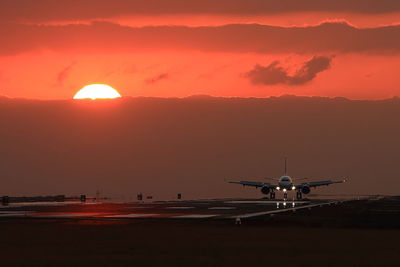 Airplane on runway against sky during sunset