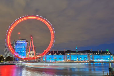 Illuminated ferris wheel in city against sky at night