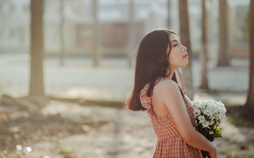 Side view of young woman holding flowers on field