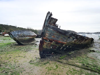 Abandoned boat moored on beach against sky