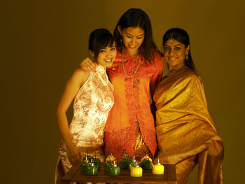 Smiling young friends with oil lamps against wall