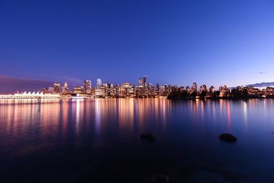 Sea by illuminated city skyline against clear sky during dusk