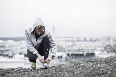 Full length of sporty woman tying shoe lace on rock