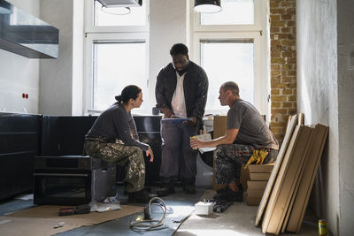 Multiracial male and female carpenters planning in kitchen at apartment