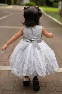 Rear view of little girl wearing frock while walking on footpath
