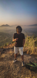 Full length of young man standing on land against sky during sunrise