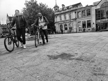 People riding bicycle on street against buildings in city