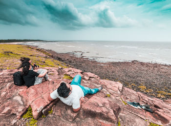 People on rocks by sea against sky