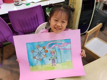 High angle portrait of smiling girl holding drawing while sitting in school