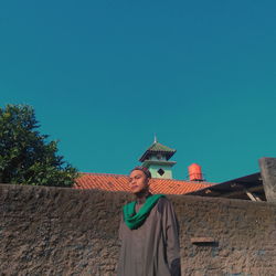 Low angle view of woman standing against building against clear blue sky