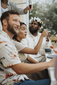 Young man toasting drink with male and female friends during dinner party at cafe