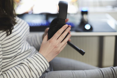 Midsection of woman holding headphones sitting by table at home