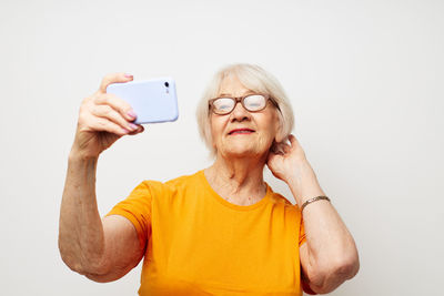 Senior woman taking selfie against white background