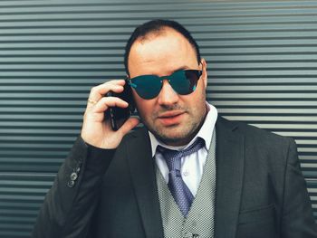 Portrait of businessman in sunglasses talking on mobile phone against wall