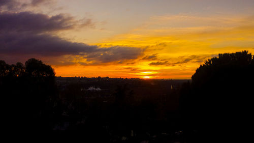 Scenic view of dramatic sky over silhouette trees during sunset