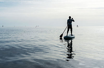 Young man on stand up paddle board on sea on sunny summer day, active lifestyle, outdoor activity